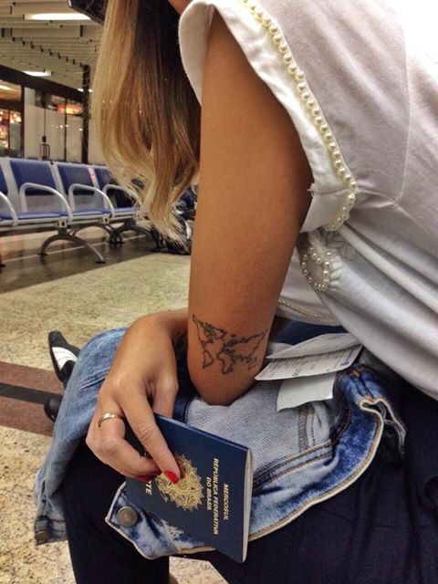 Tatuagem de mapa mundi nos braços de uma mulher sentada no aeroporto.