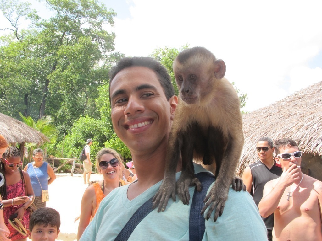 Macaco prego no ombro de um homem jovem e sorridente.