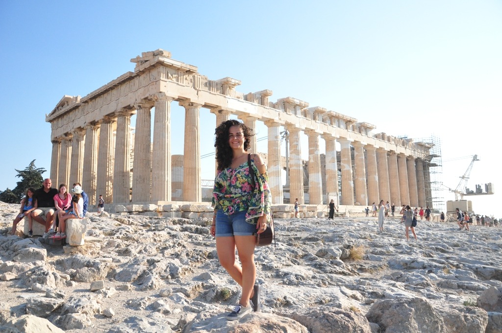 Mulher em primeiro plano, pantheon no fundo com um céu azul. Foto que ilustra o artigo quando ir para a Grécia, já que mostra vários outros turistas ao fundo. 