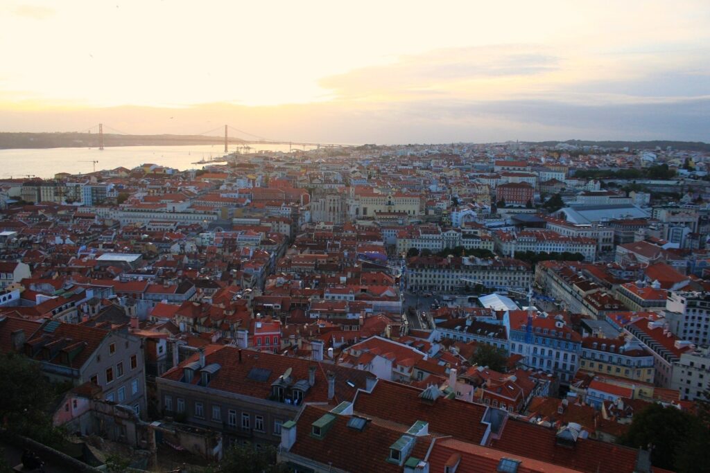 Vista da cidade de Lisboa, um rio no canto superior esquerdo e a cidade ao entardecer.