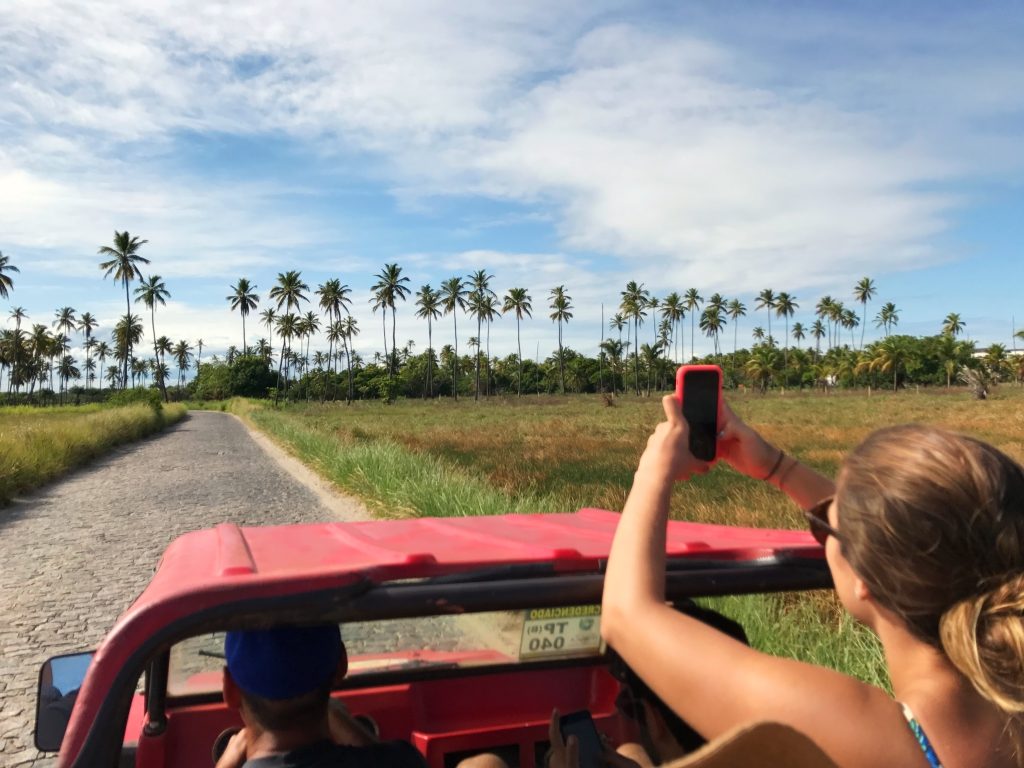 Menina no buggy tira foto do caminho a frente e do horizonte com coqueiros. 