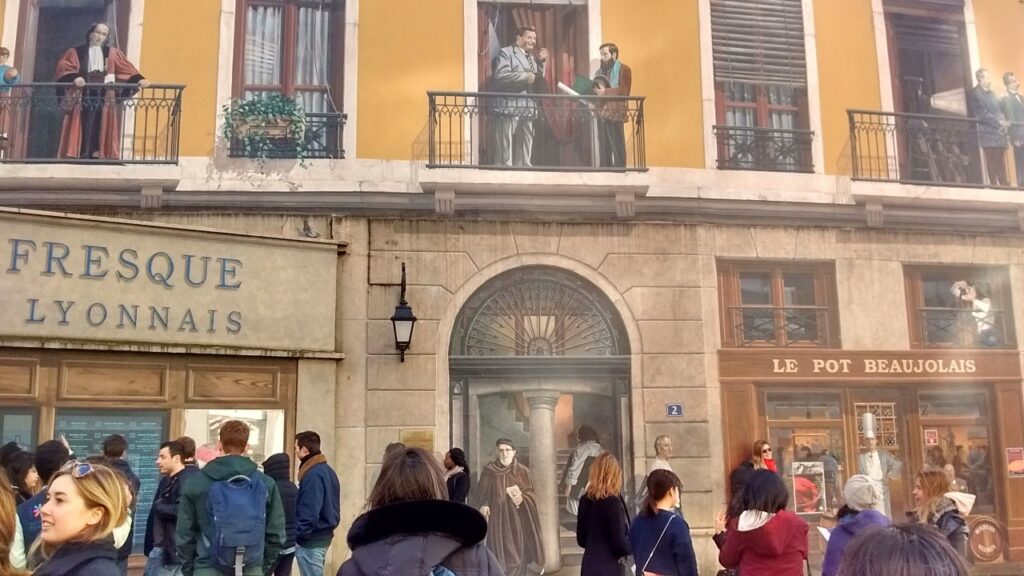 Pessoas e pinturas se misturam confundindo quem passa na frente da Fresque des Lyonnais Celèbres.