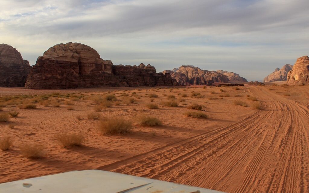 Foto da areia do deserto, em que há marcas de pneus demarcando o caminho que o jipe deve seguir. 