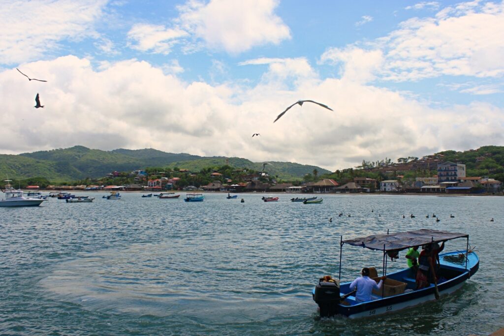 Nicarágua, no vilarejo de San Juan del Sur, barco cruza o mar, enquanto um pássaro sobrevoa em um céu azul