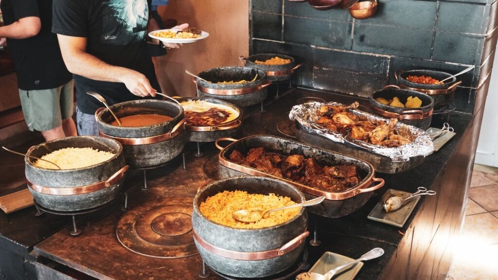 Buffet de comida caseira servido em panelas de pedra cinzas com detalhes em cobre. São 5 pratos em cada lado. 