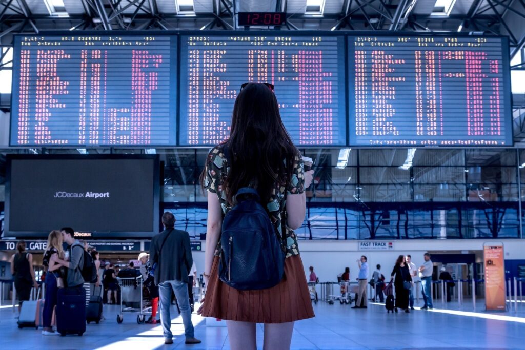 Mulher de costas no centro da imagem olha painel de destinos em aeroporto