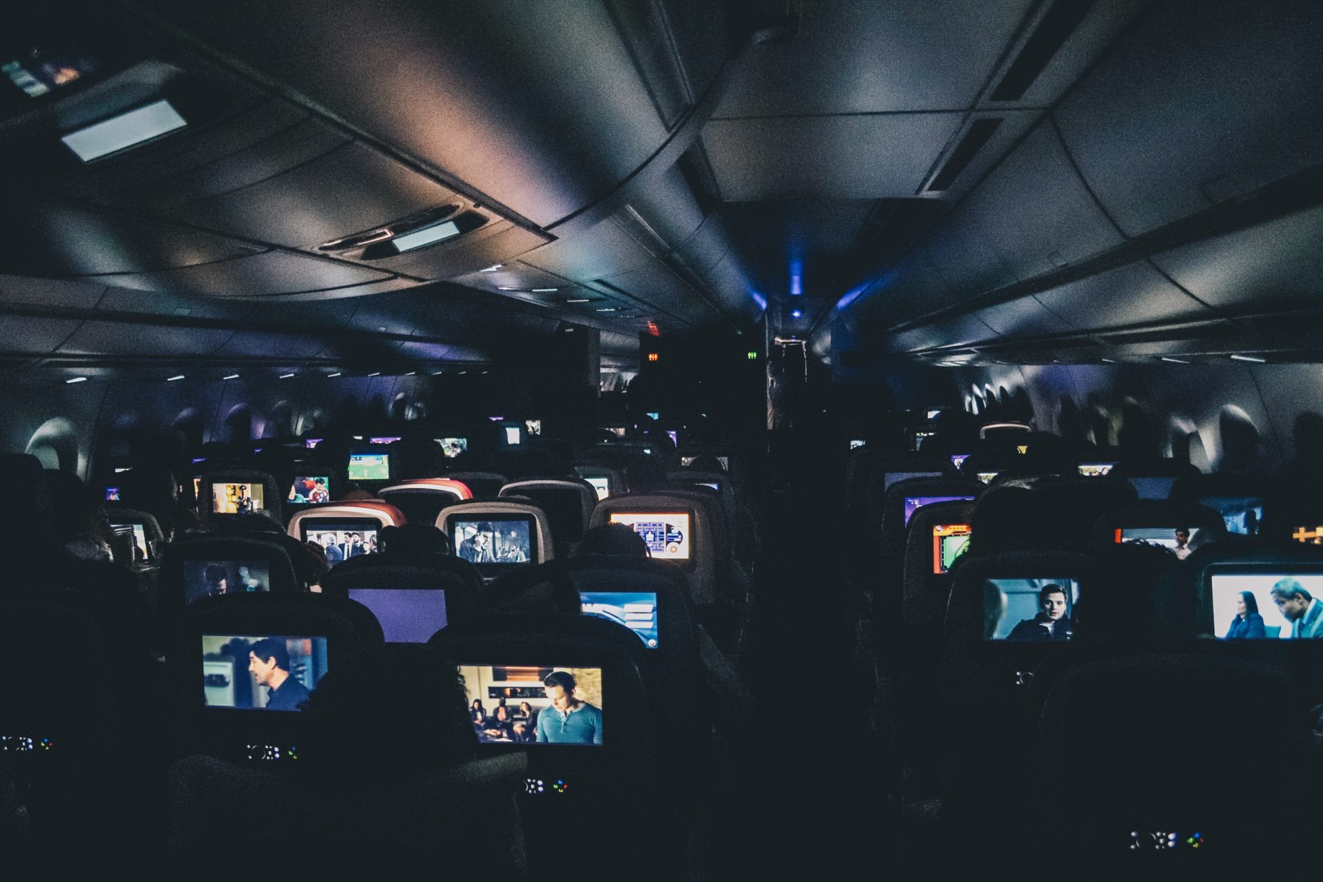 Foto tirada dos fundos de um avião no escuro, com todas as tvzinhas acesas com alguma coisa passando