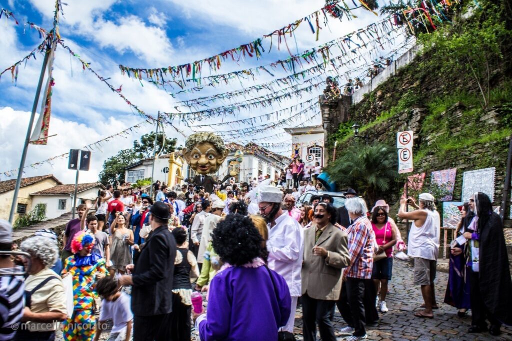 Pessoas fantasiadas na rua em Ouro Preto, onde há bandeirinhas cobrindo a rua