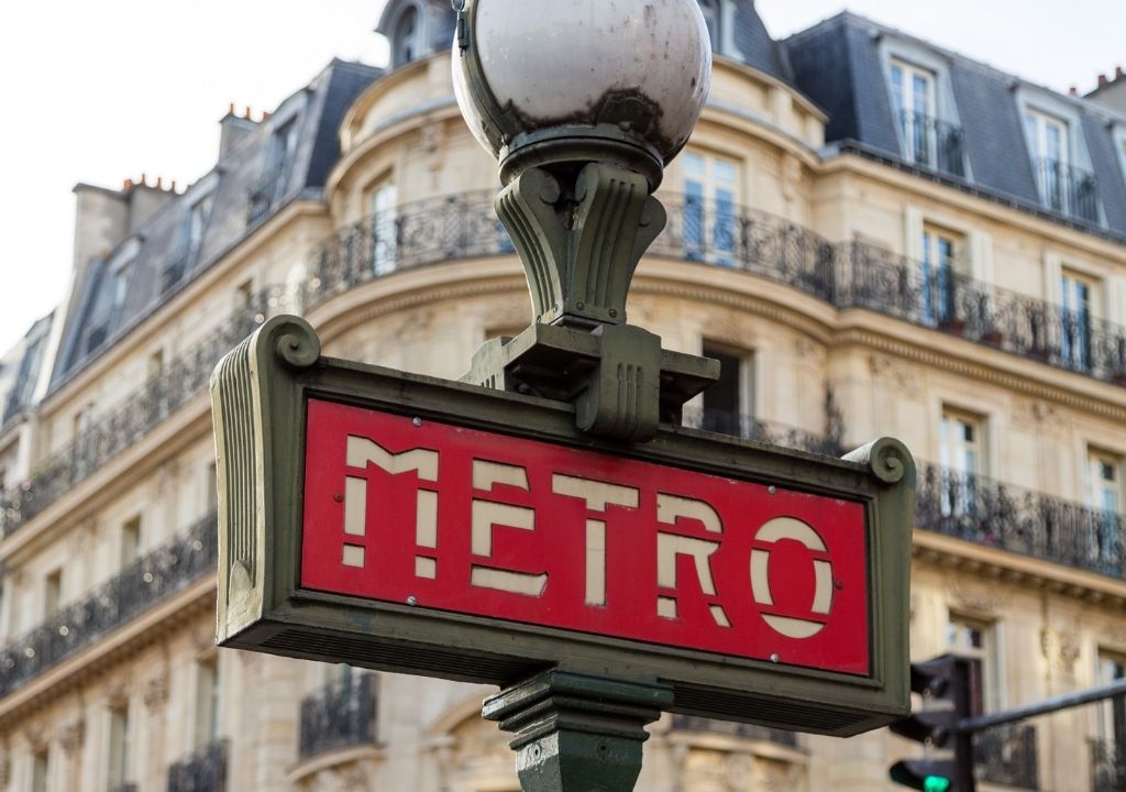 Placa sinalizando o metrô de Paris com uma construção antiga ao fundo